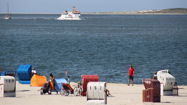 A beach with numbered beach chairs and a boat in the water. - Apartment in a Quiet Location in Dornumersiel (Dornum)