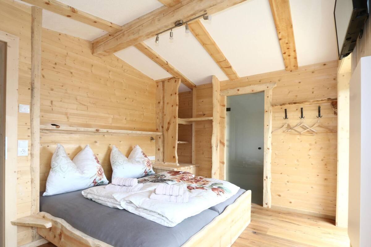 A wooden cabin bedroom with a bed, pillows, a wardrobe, and a door.