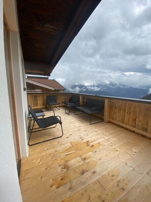 Une terrasse en bois avec des sièges extérieurs et une vue sur les montagnes.