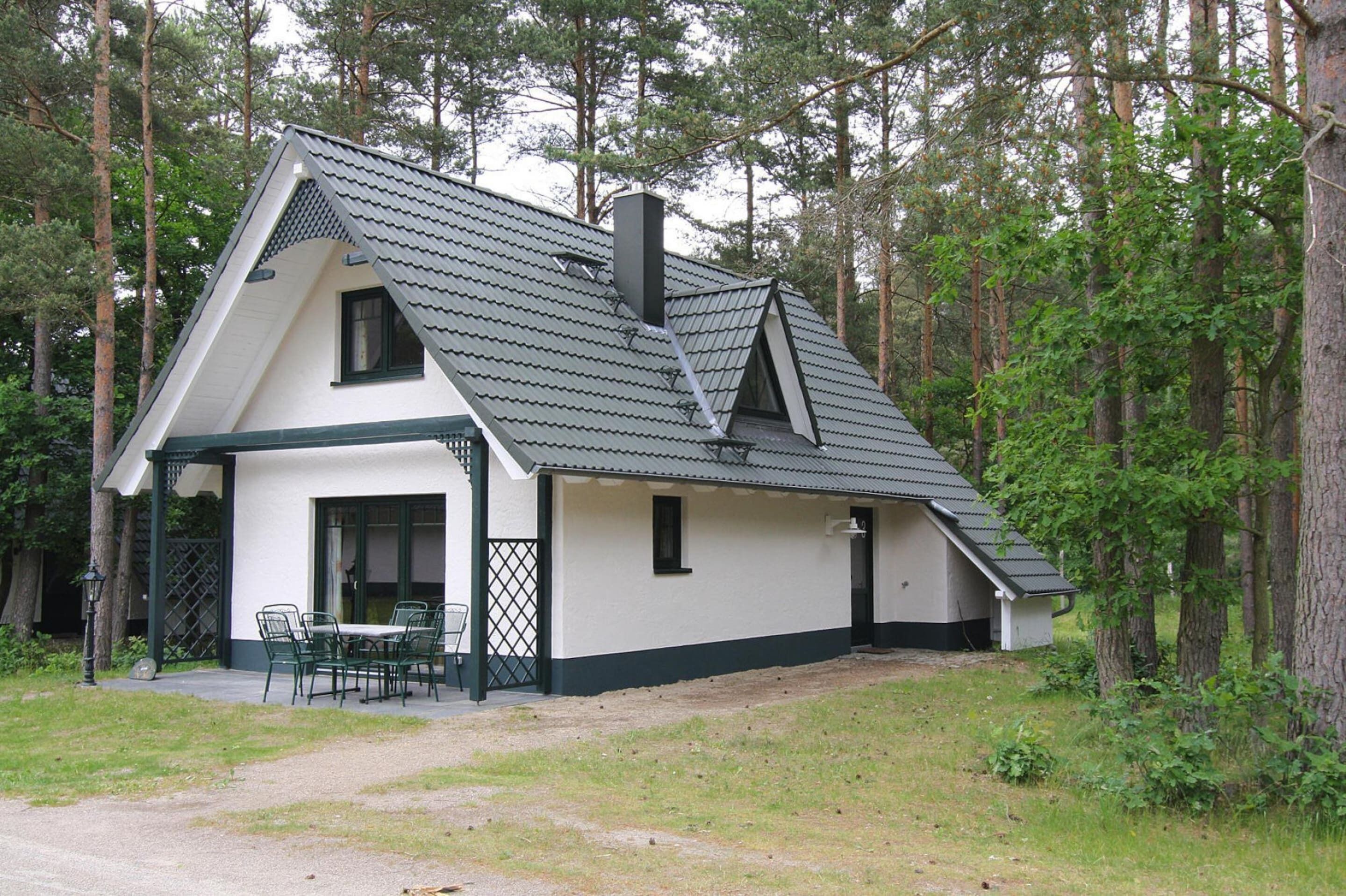 A two-story house with a steeply pitched roof, a chimney, and a small porch with chairs.
