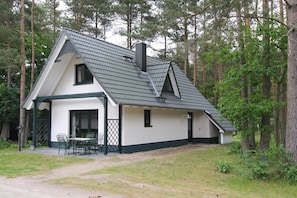 Ett tvåvåningshus med ett brant tak, en skorsten och en liten veranda med stolar.