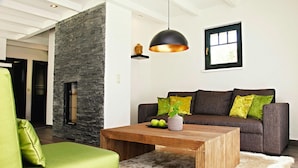 A modern living room with a stone accent wall, a wooden coffee table, a green sofa, and a grey couch with green and yellow cushions. - Semi-detached Houses at the Drewitzer See, Drewitz (Nossentiner Huette)
