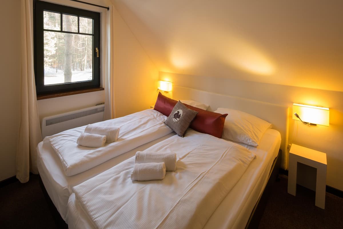 Een hotelkamer met twee bedden, elk voorzien van witte lakens en handdoeken, een raam met uitzicht op bomen en nachtlampjes.