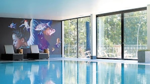 An indoor swimming pool with a mural, lounge chairs, and large windows offering a view of the outdoors. - Semi-detached Houses at the Drewitzer See, Drewitz (Nossentiner Huette)