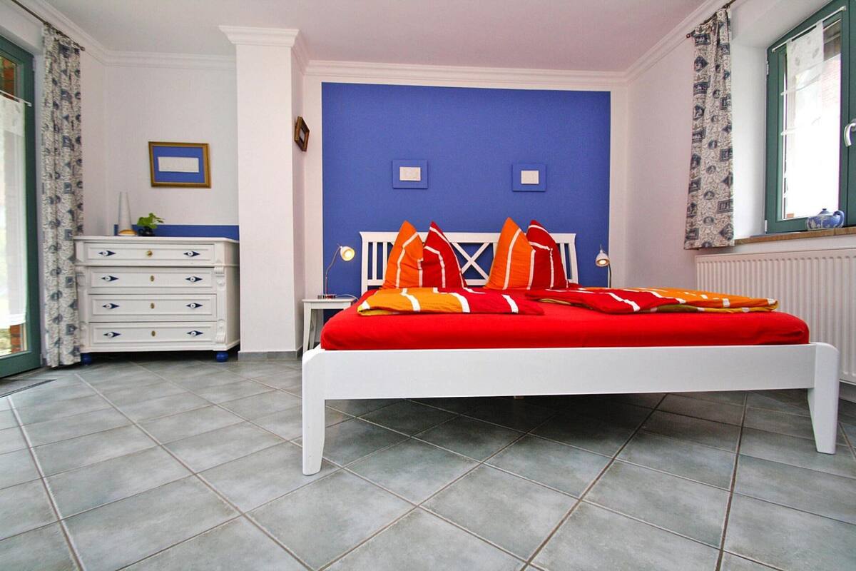 A bedroom with a white bed, red bedding, a white dresser, and a blue accent wall.