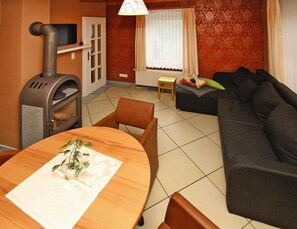 A living room with a sofa, a table with a plant, a fireplace, and a television on a shelf. - Holiday Home, Plau am See (Plau am See)