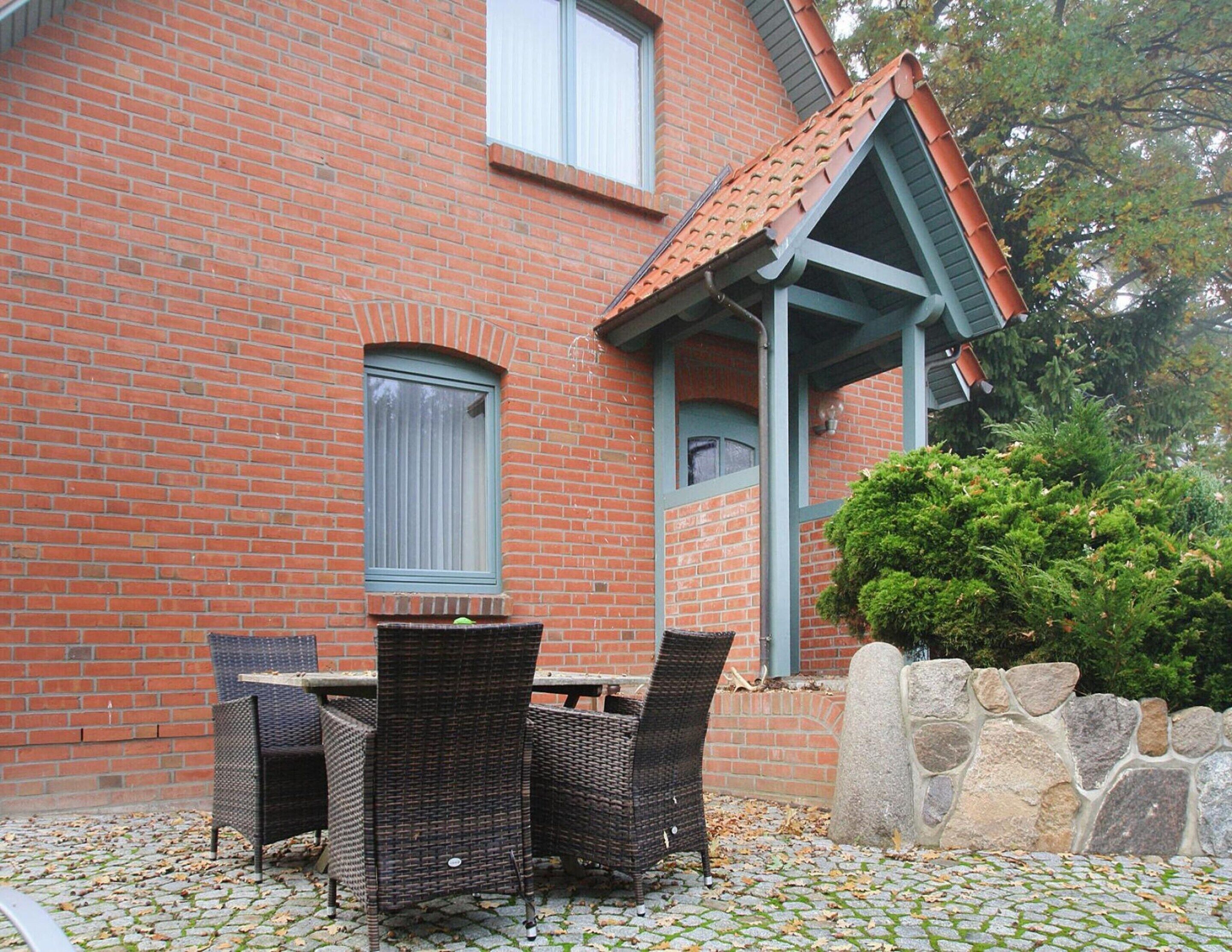 A brick building with a tiled roof, a stone wall, and a small garden area with a table and chairs.