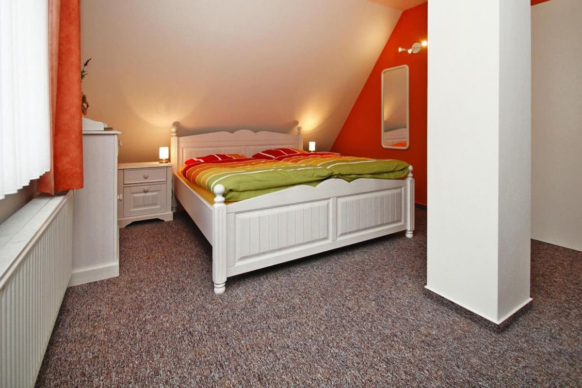 A bedroom with a white bed, a nightstand, a lamp, and a radiator.