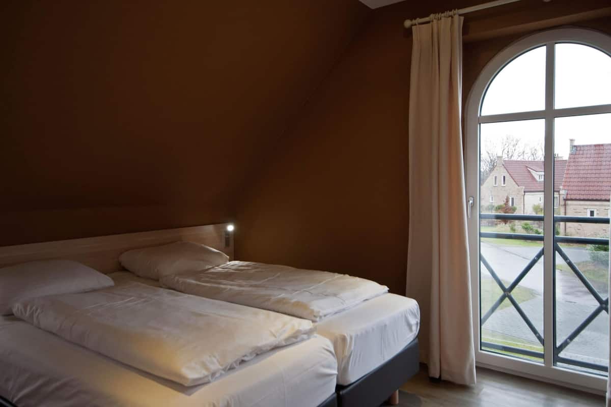 A bedroom with two beds, a large window, and a view of the outside.