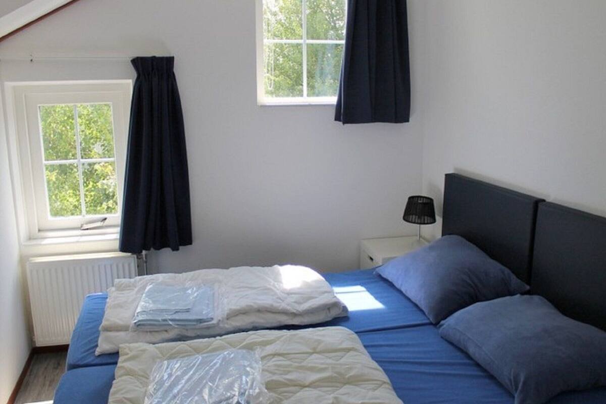 A bedroom with two beds, a window with curtains, a bedside lamp, and a radiator.