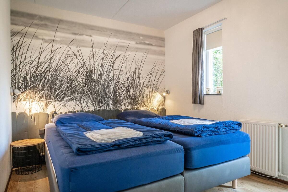 A bedroom with two beds, a wooden floor, a window, and a wall with a decorative plant arrangement.