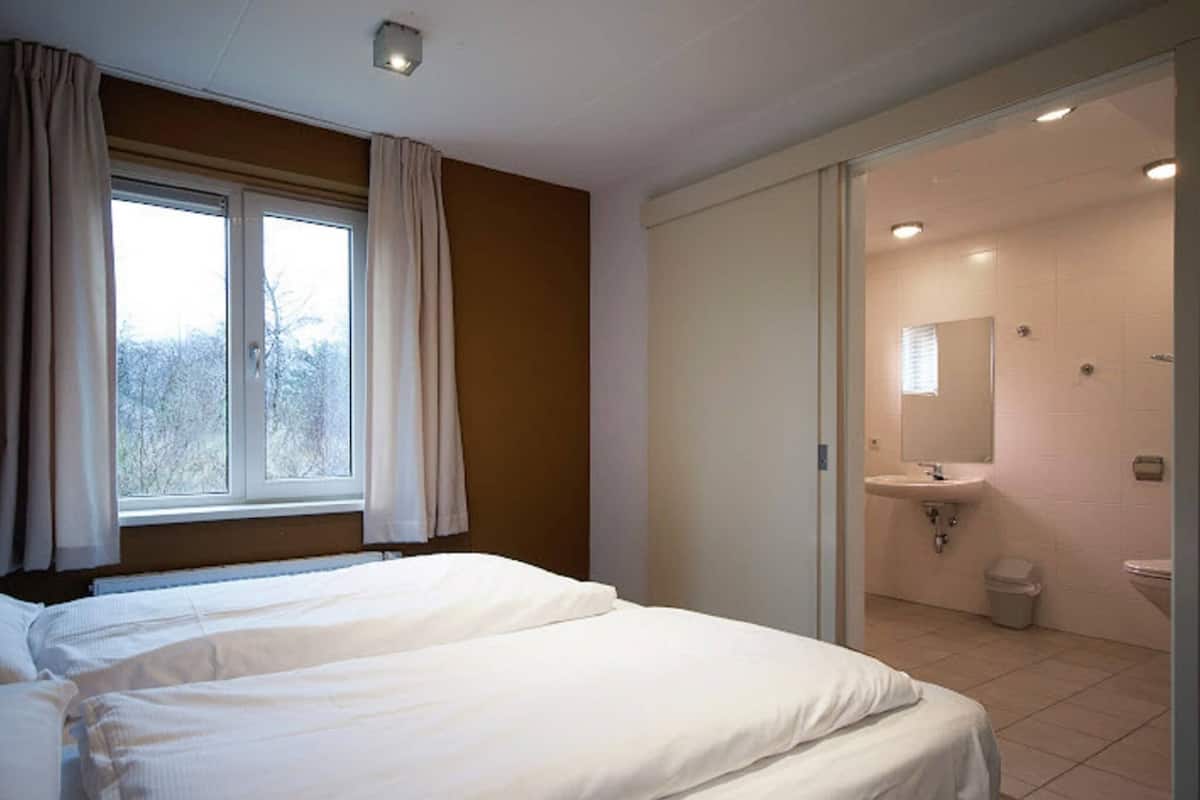 A bedroom with a large bed, a window with curtains, and a bathroom visible through an open door.