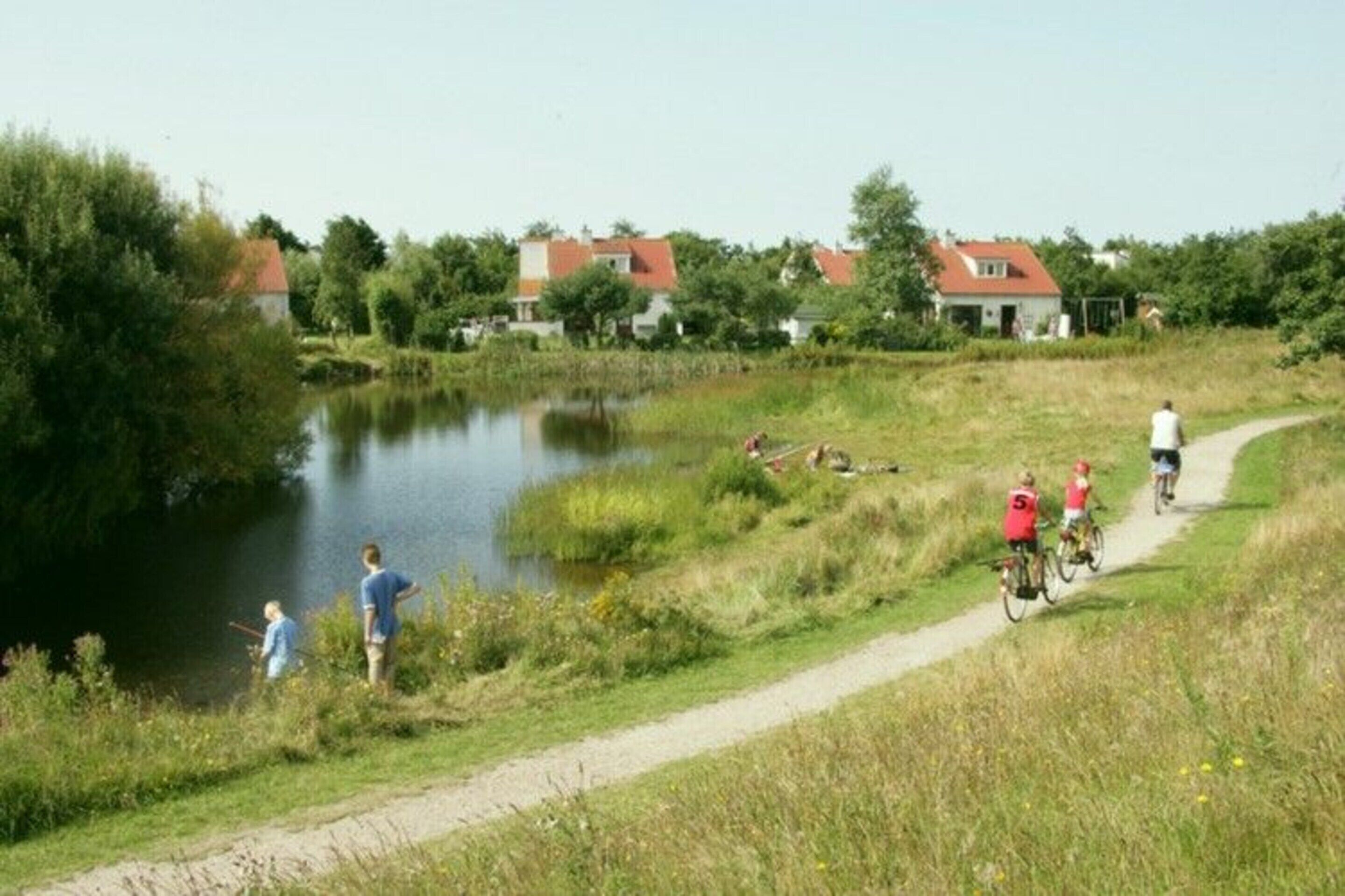 A pathway beside a pond with houses in the background.
