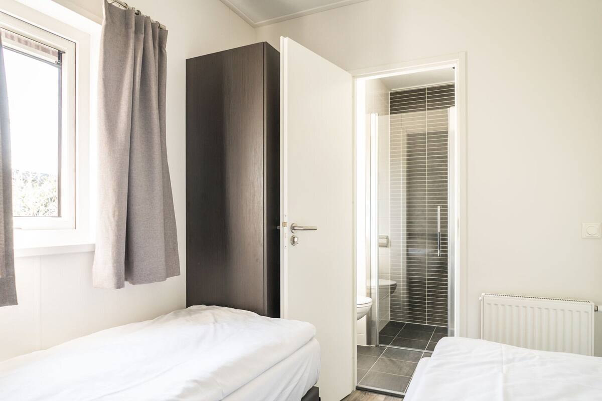 A modern bedroom with two beds, a wardrobe, and a bathroom with a shower.