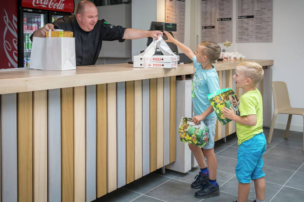 A counter with a Coca-Cola refrigerator, a menu board, and a pizza box on the counter.