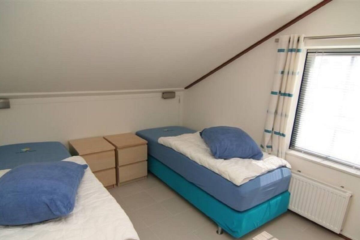 A small, simple room with two beds, a window with blinds, and a radiator.