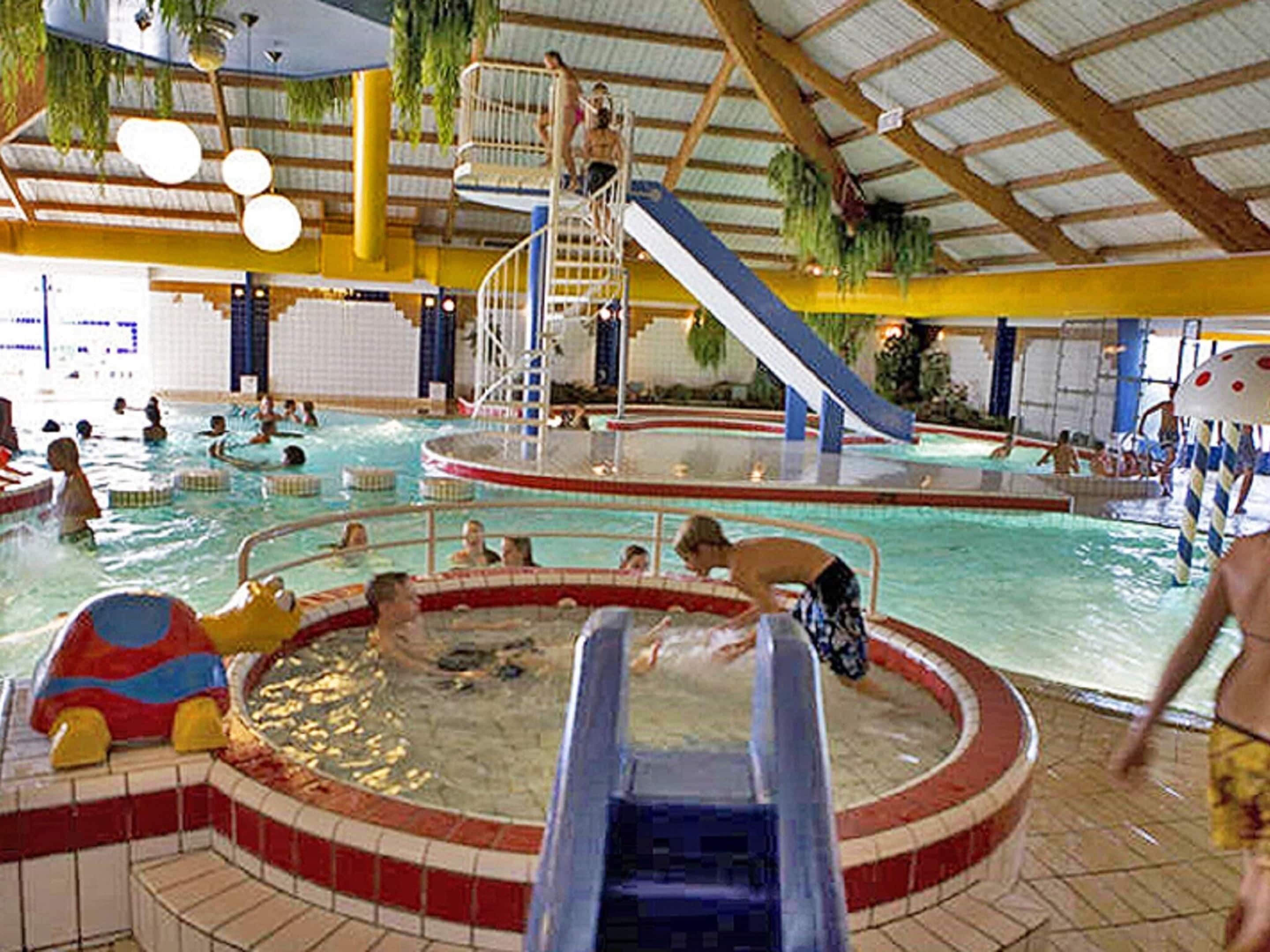 Een binnenzwembad met verschillende waterglijbanen, een jacuzzi en een zwembadgedeelte waar mensen zwemmen en spelen.