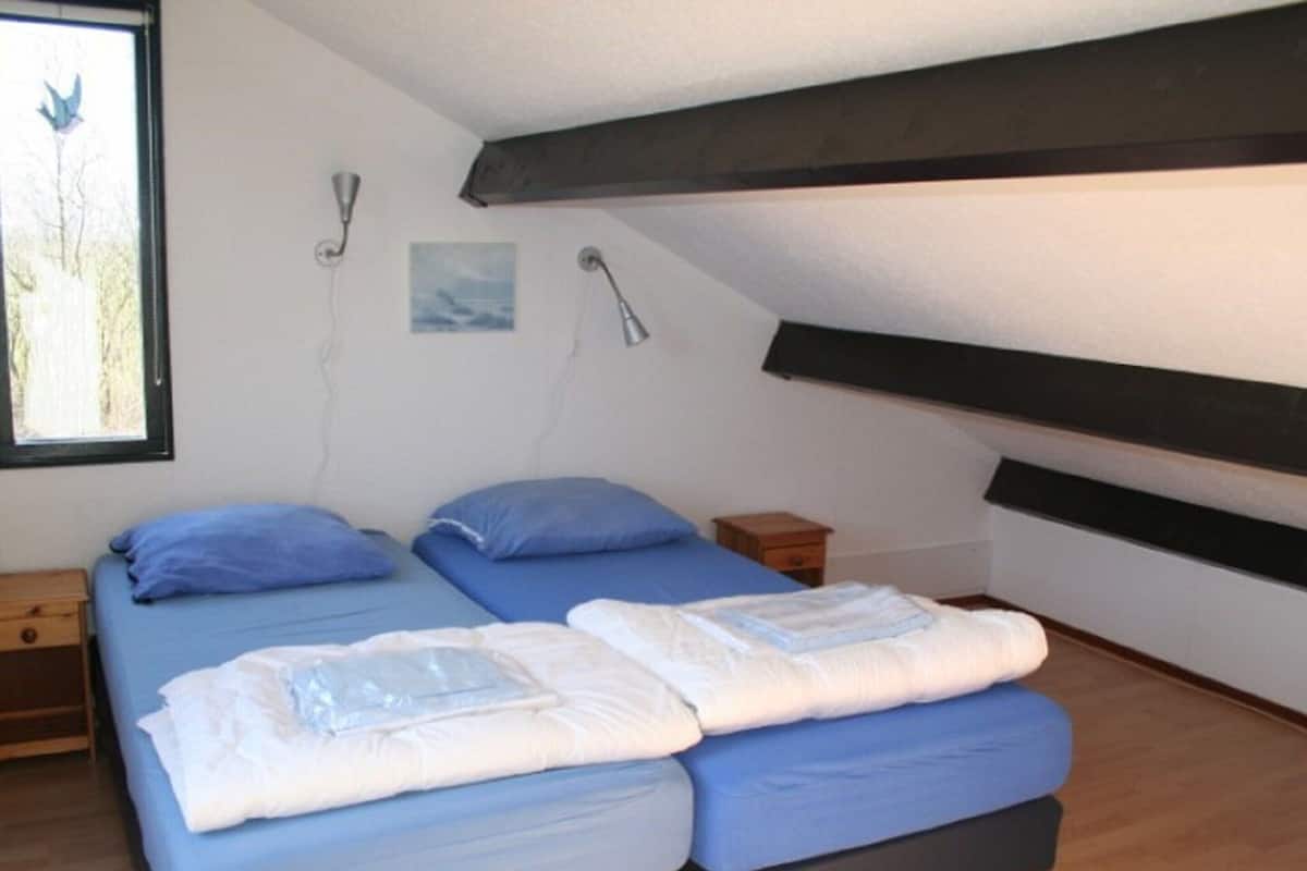 A room with two beds, a window with a view of trees, and a painting on the wall.