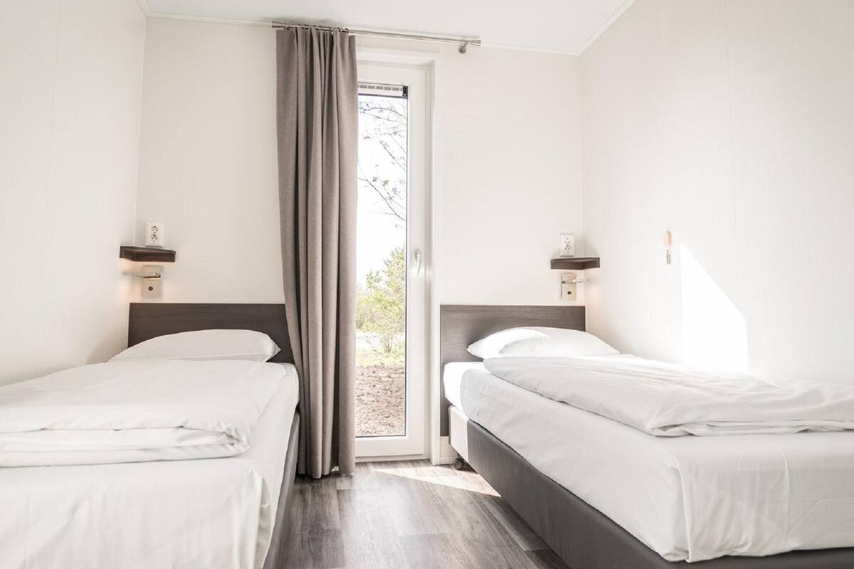 A hotel room with two single beds, a sliding glass door, and a view of the outdoors.