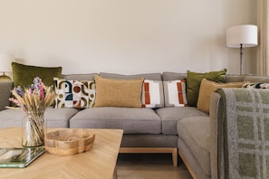 A modern living room with a grey sofa, a wooden coffee table, and a vase of dried flowers.