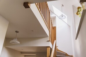 A staircase with wooden railings and a white wall. There is a hanging light fixture and a vase with flowers on the wall.