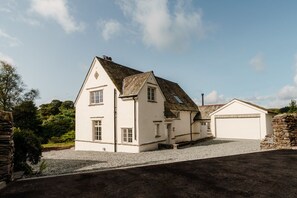 Stunning country house with a central entrance, flanked by windows and a dormer window, set amidst a rural landscape.