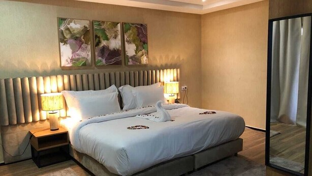 A modern hotel room with a large bed, two bedside lamps, a headboard with vertical slats, and abstract wall art. - Hotel Hariz Son (Berrechid)