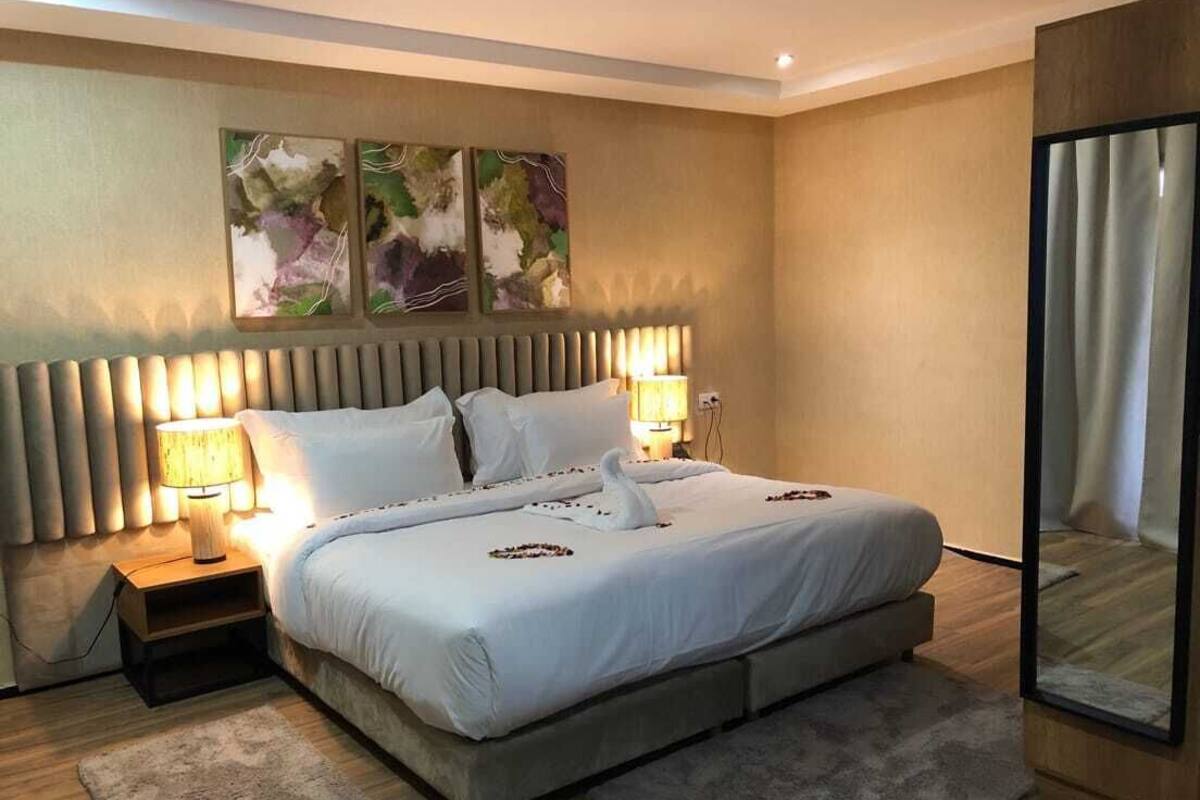 A modern hotel room with a large bed, two bedside lamps, a headboard with vertical slats, and abstract wall art.