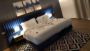 A hotel room with a bed, a headboard, a nightstand, a lamp, a patterned rug, and artwork on the wall. - Hotel Hariz Son (Berrechid)