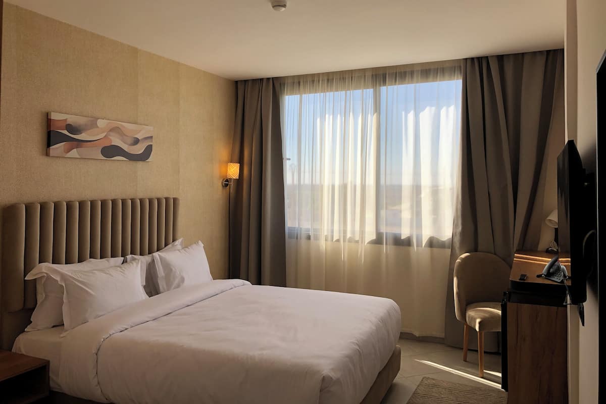 A hotel room with a large bed, a desk with a telephone, and a chair.