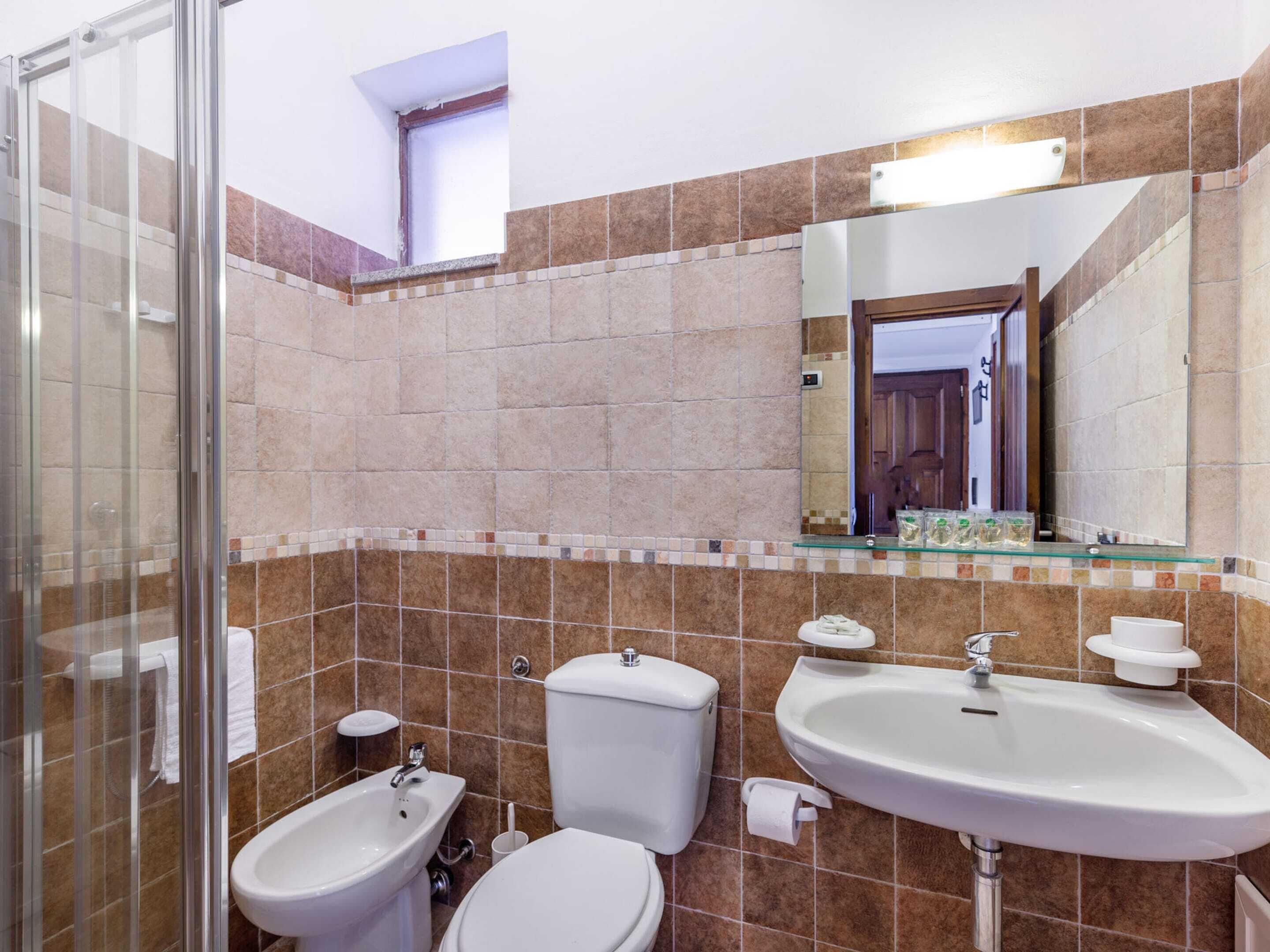 A bathroom with a glass shower enclosure, a toilet, a bidet, and a sink with a mirror above.