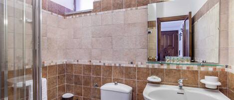 A bathroom with a glass shower enclosure, a toilet, a bidet, and a sink with a mirror above.