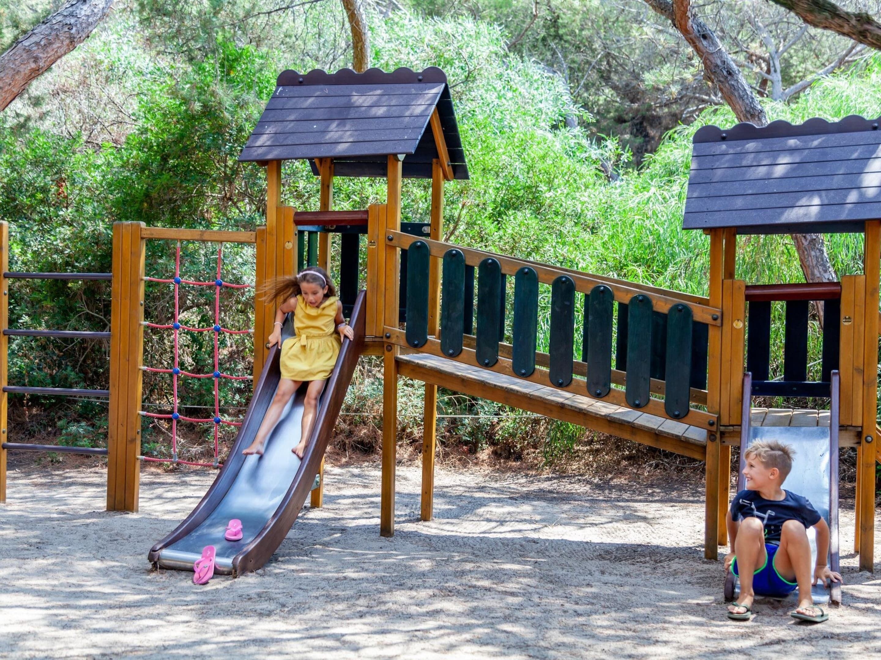 A playground with a slide, climbing net, and a seesaw.