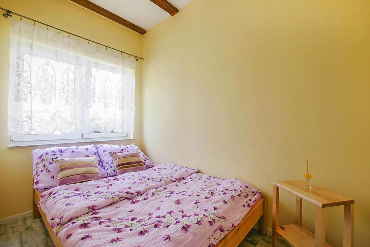 Une chambre à coucher avec un lit, une fenêtre avec des rideaux légers et une table de chevet.