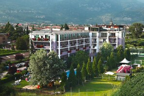 A multi-story hotel with balconies, a swimming pool, and a view of the surrounding town and mountains. - Apartment in Riva del Garda (Riva del Garda)