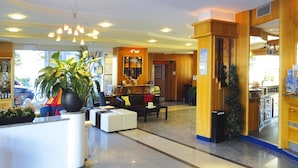 A hotel lobby with a reception desk, seating area, and a large potted plant.