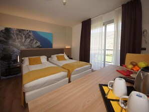 A hotel room with two beds, a wooden desk, a fruit bowl, and a painting on the wall. - Apartment in Riva del Garda (Riva del Garda)