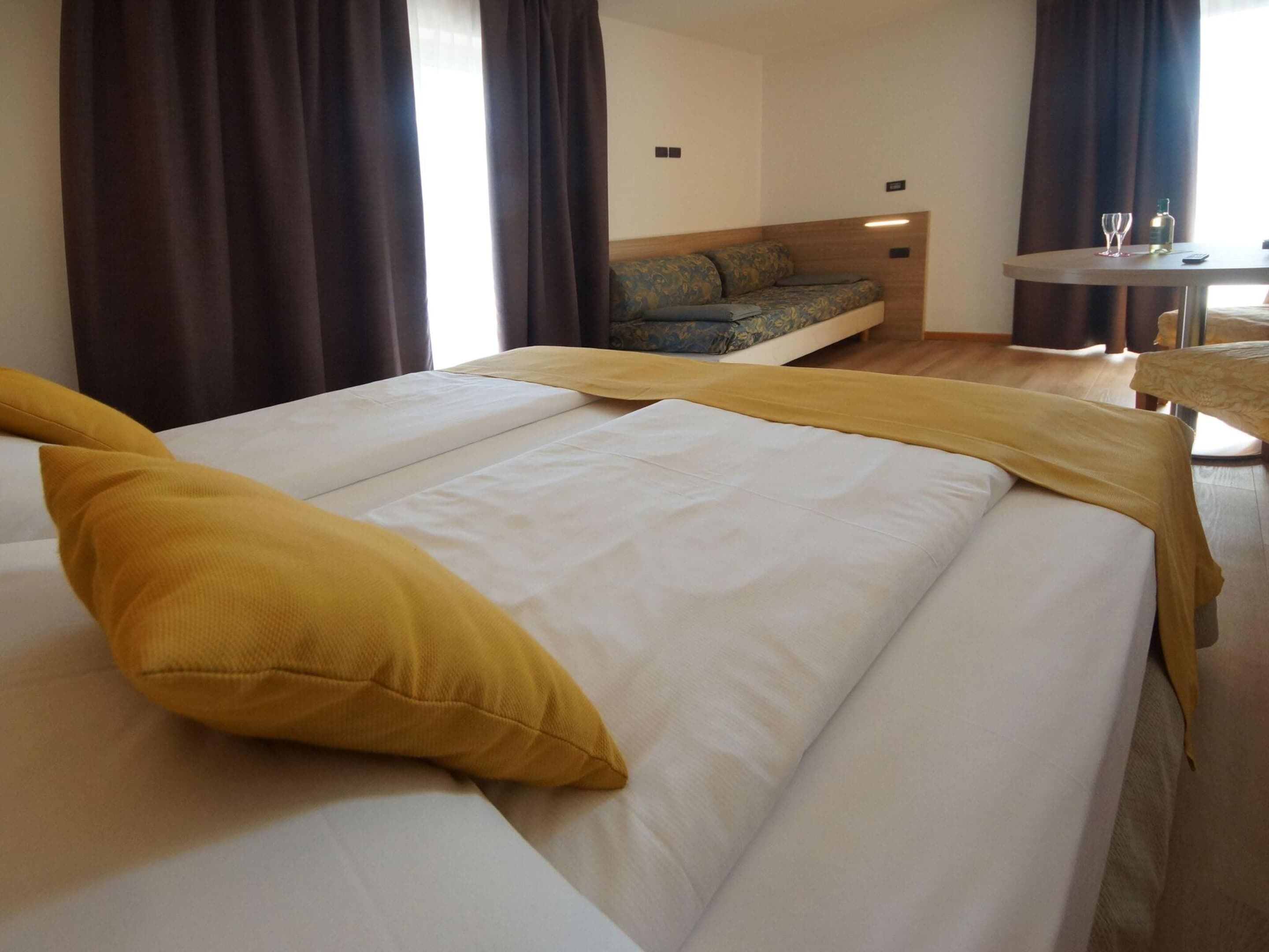 Une chambre d’hôtel avec un lit, une petite table sur laquelle se trouvent un verre et une bouteille, et un canapé à l’arrière-plan.