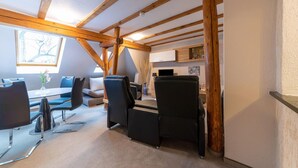 Une chambre moderne de style loft, avec des poutres apparentes en bois, un coin repas avec des chaises noires, un canapé et une petite table sur laquelle est posé un vase.