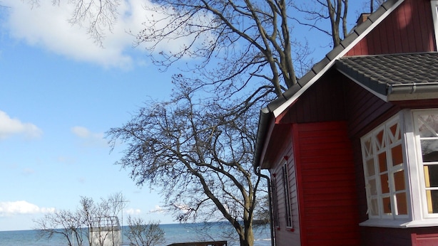 Un bâtiment rouge avec vue sur la mer. On y trouve des tables et des chaises en bois à l’extérieur.