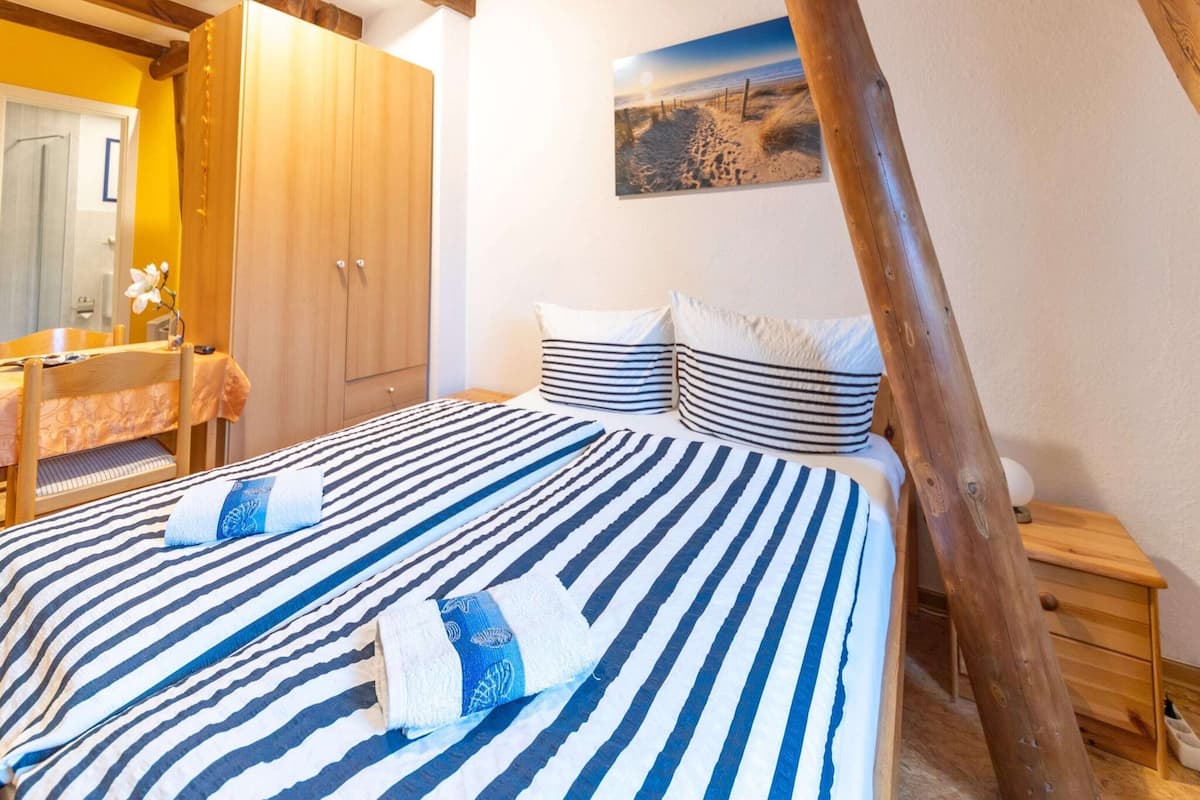 Een slaapkamer met een bed, strepenbeddengoed, een houten garderobe, een nachtkastje en een schilderij aan de muur.