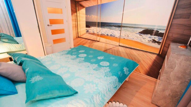 Een slaapkamer met een bed, uitzicht op het strand en een deur met geëtste glaspanelen.