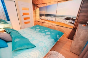 A bedroom with a bed, a view of the beach, and a door with frosted glass panels.