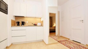 Een moderne keuken met witte kasten, een magnetron en een koffiezetapparaat. Er is een houten aanrecht en een vloerkleed dat naar een slaapkamer leidt.