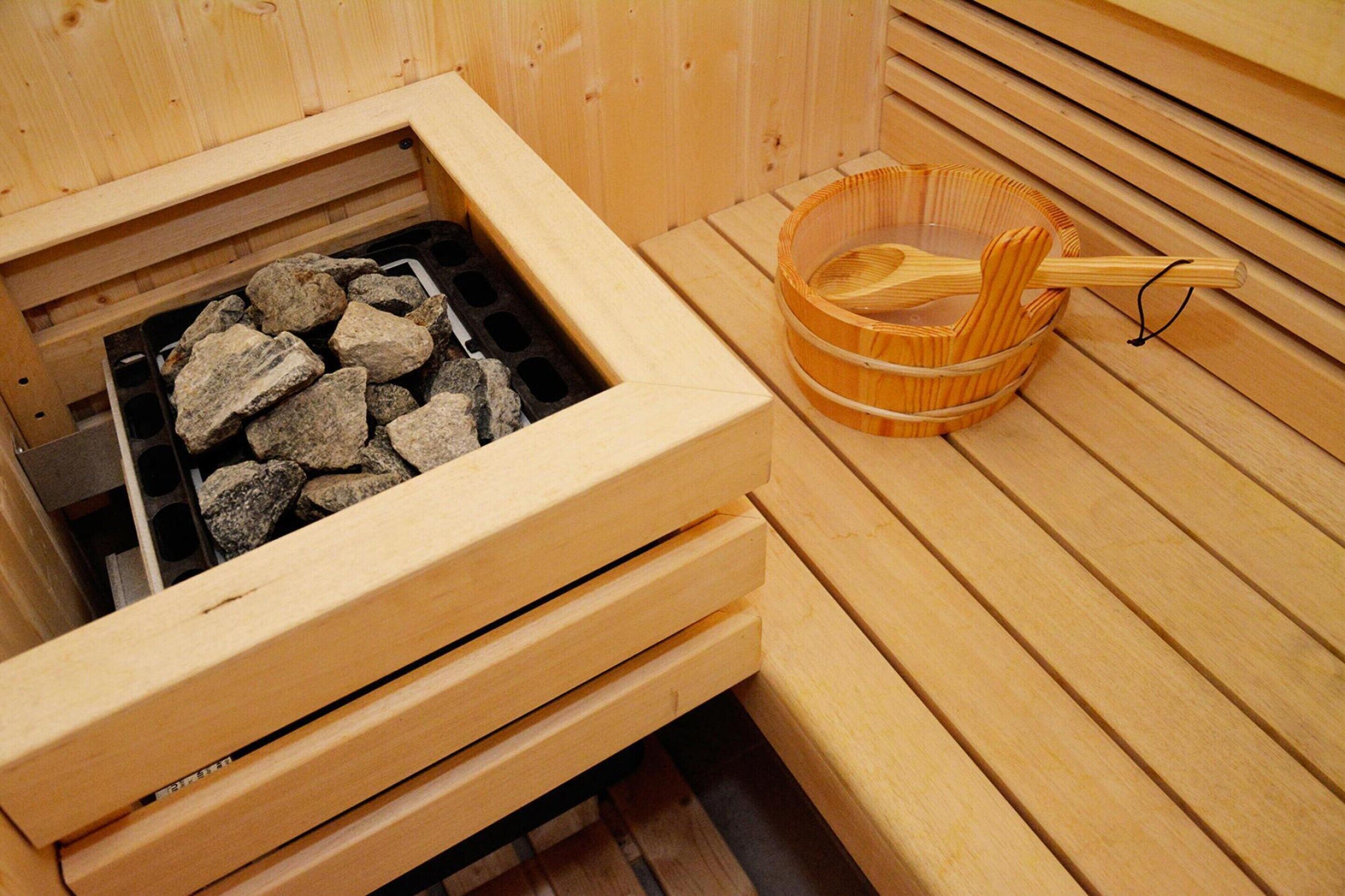 A sauna with a wooden bench, a stone-filled heating element, and a wooden bucket with a ladle.