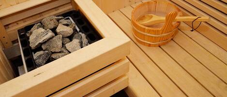 A sauna with a wooden bench, a stone-filled heating element, and a wooden bucket with a ladle.