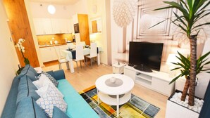 Een moderne woonkamer met een blauwe bank, een ronde salontafel en een flatscreen televisie.