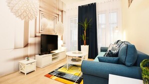 Een moderne woonkamer met een flatscreen televisie, een blauwe bank, een klein wit bijzettafeltje, een decoratieve lamp en een potplant.