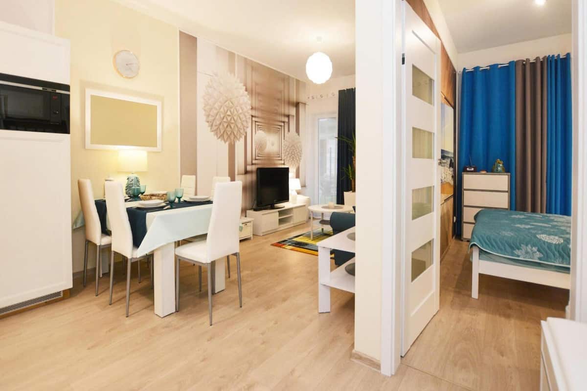 Ein modernes, helles Zimmer mit Essecke, Fernseher und Bett.