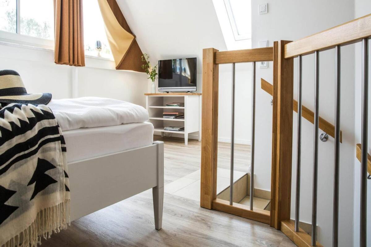 A modern bedroom with a sloped ceiling, a bed, a TV, and a wooden staircase.